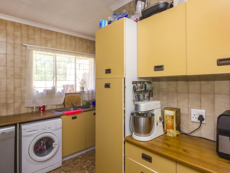 A functional kitchen featuring dated cabinetry, laminate countertops, a double basin sink, and tiled backsplash, offering potential for modernization.