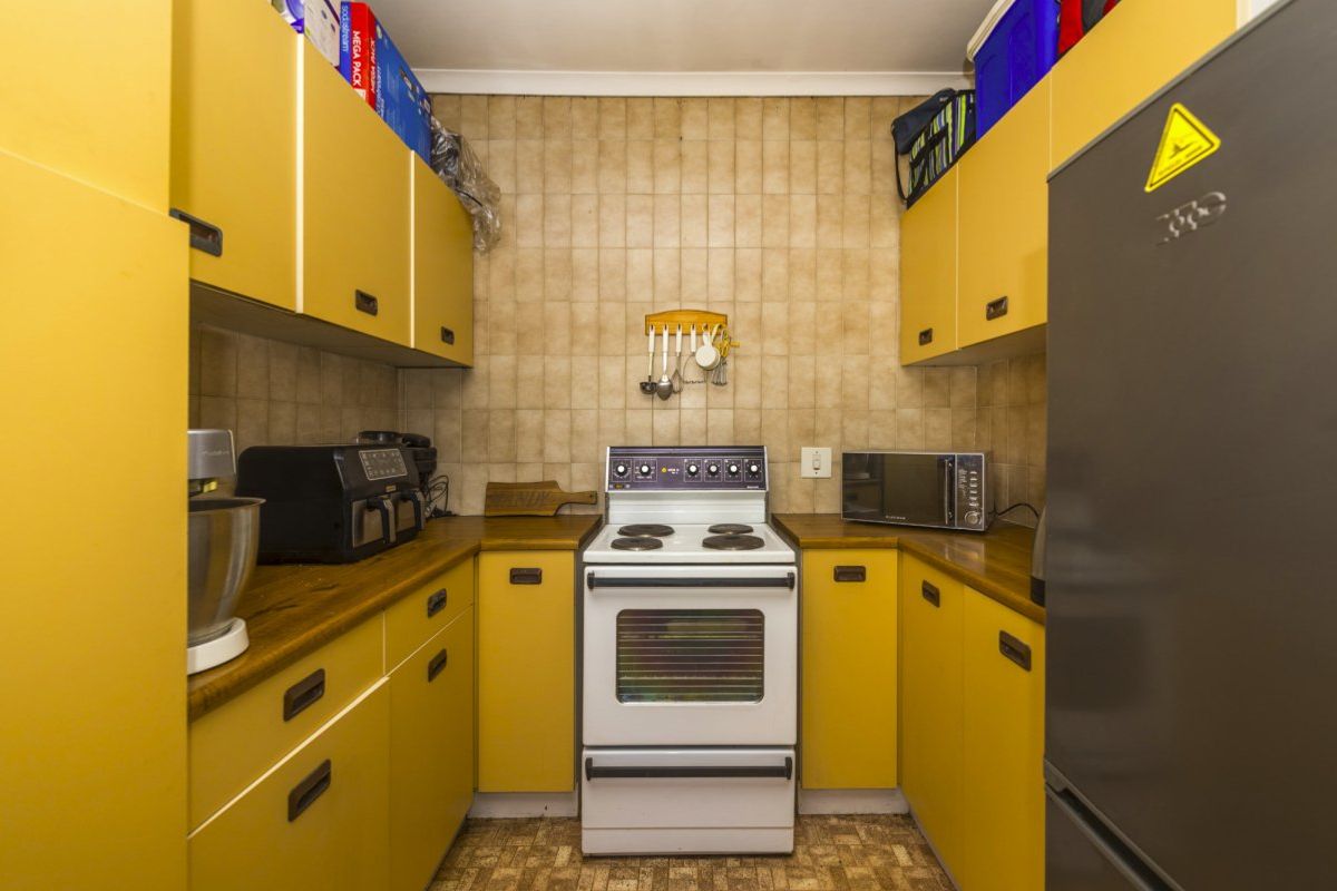 Compact galley-style kitchen featuring dated yellow cabinetry, laminate countertops, and a freestanding stove with tiled backsplash.
