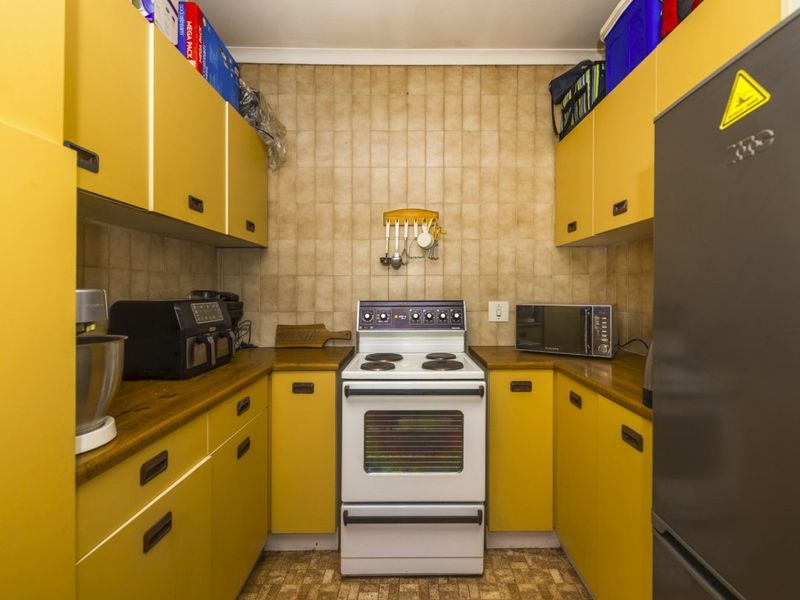 Compact galley-style kitchen featuring dated yellow cabinetry, laminate countertops, and a freestanding stove with tiled backsplash.