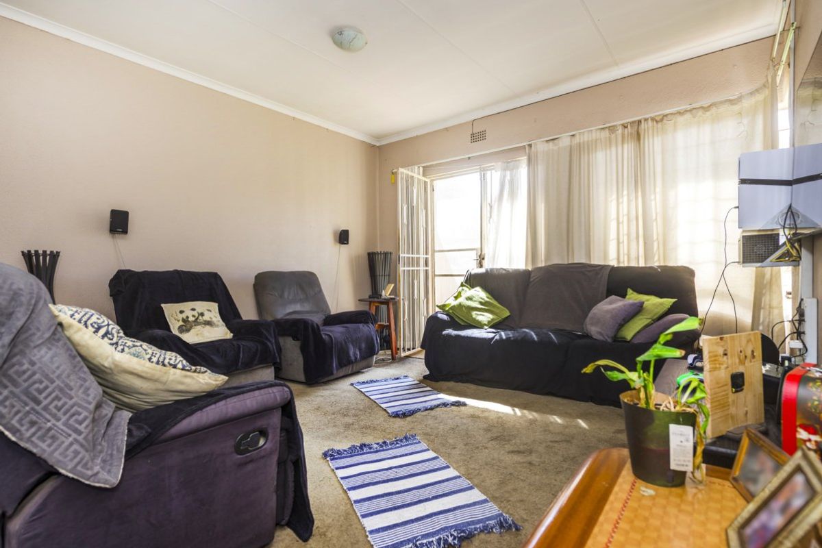 A living room featuring carpet flooring and a sliding door with a security gate, providing access to the exterior.