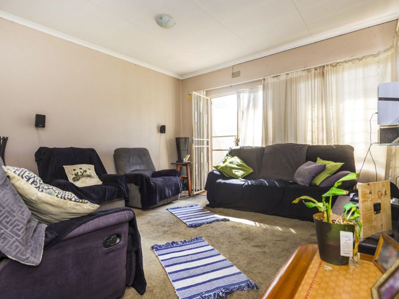 A living room featuring carpet flooring and a sliding door with a security gate, providing access to the exterior.