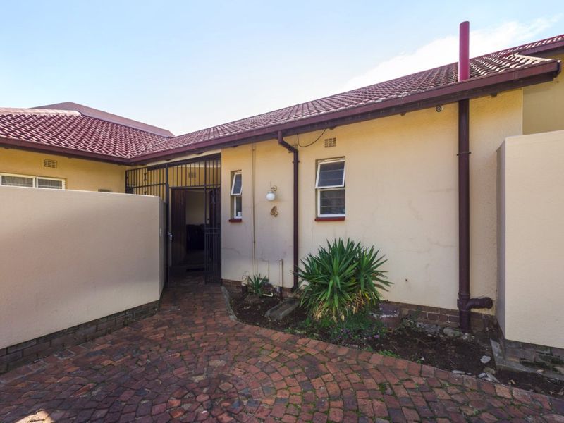 Front entrance area of the townhouse featuring a brick paved courtyard, security gate, and tiled roof structure.