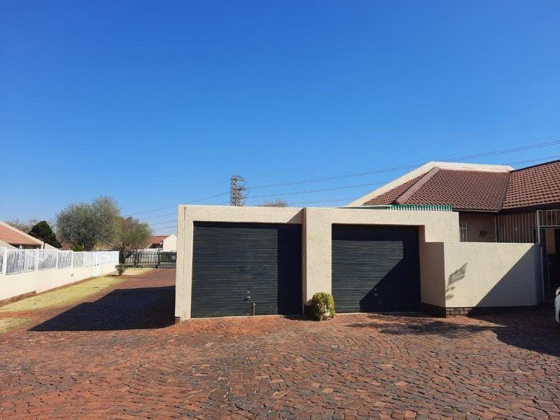 Exterior view of a townhouse property featuring a double garage with dark roller doors and a spacious paved driveway.