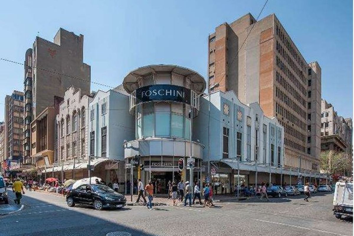 A prominent commercial building facade featuring a curved corner entrance, large display windows, and a protective canopy at street level.