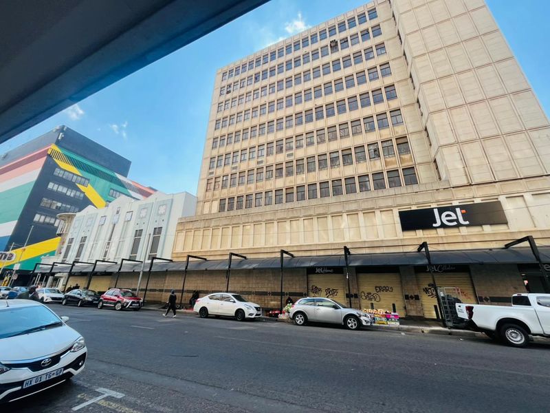 Street-level view of a multi-story commercial building featuring a retail storefront with roller shutter doors and an overhead awning.