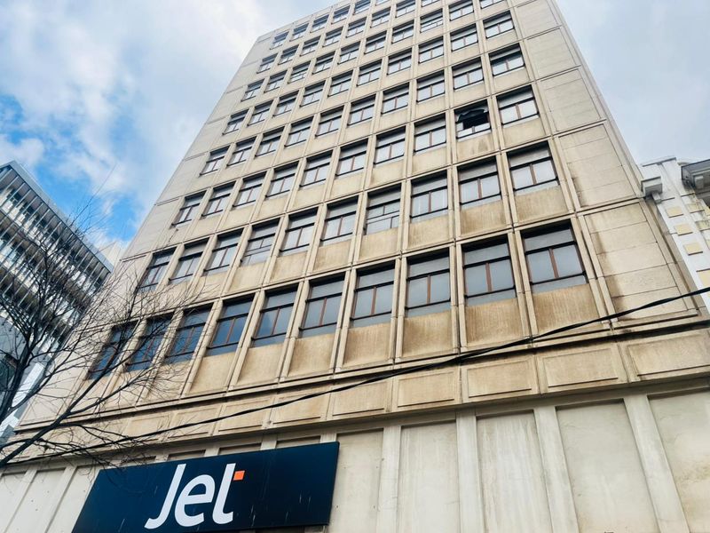 A low-angle view of a multi-story commercial building featuring a concrete facade and a grid of windows with visible exterior weathering.