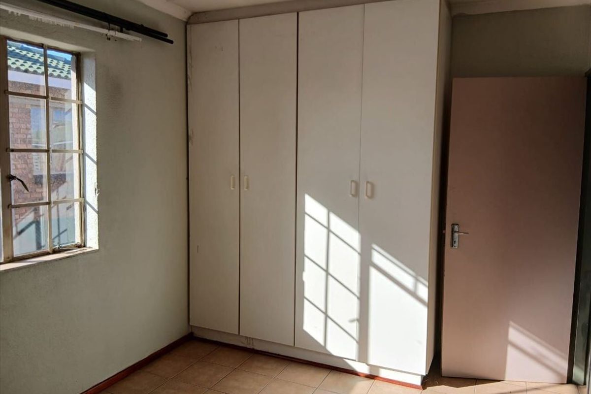 An empty bedroom featuring built-in cupboards, tiled flooring, and a steel-framed window, offering a blank canvas for renovation.