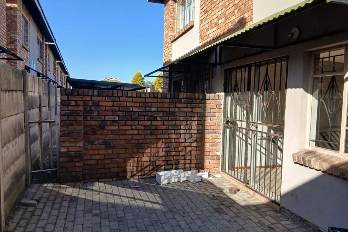 A private rear courtyard featuring paved flooring, a brick boundary wall, and a secure metal gate entrance to the townhouse.
