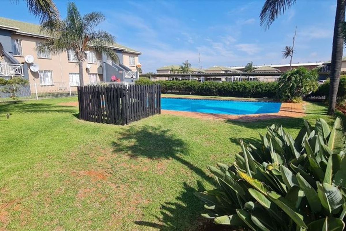 Communal outdoor area featuring a swimming pool, well-maintained lawn, and established landscaping within a residential townhouse complex.