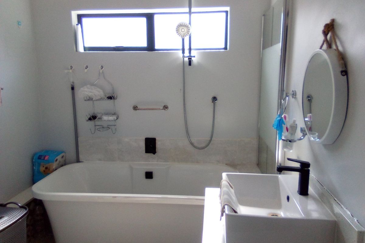 A modern bathroom featuring a freestanding bathtub, a separate shower area with a glass screen, and a contemporary basin with a black mixer tap.