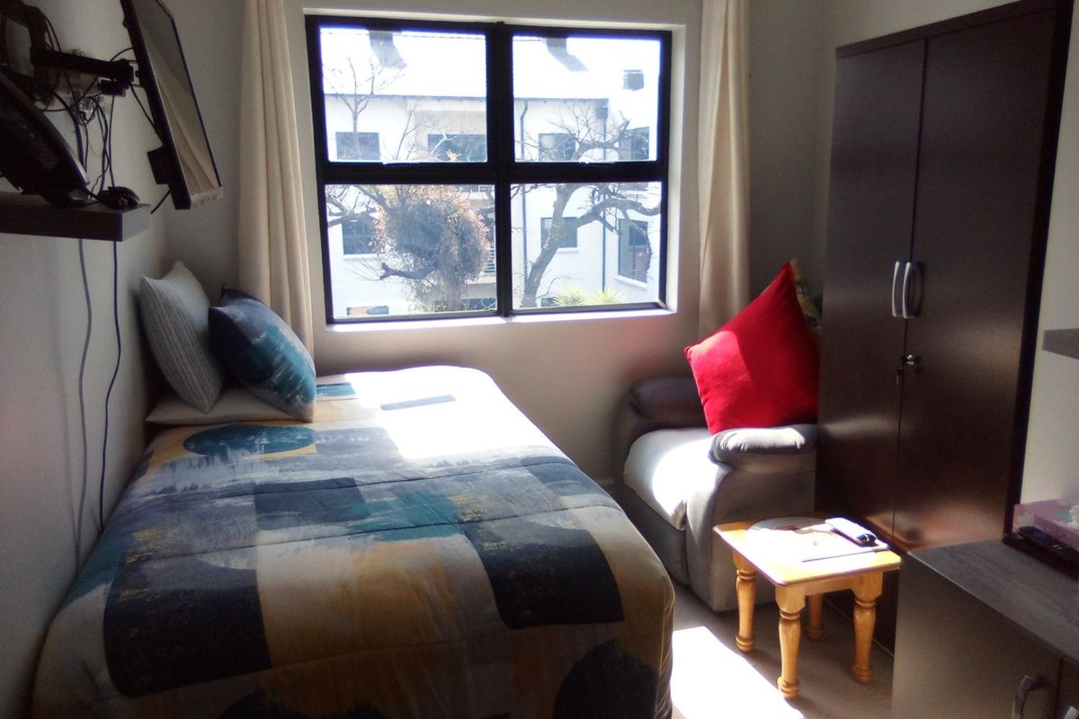 A compact bedroom featuring a built-in wardrobe and a large window that provides natural light.