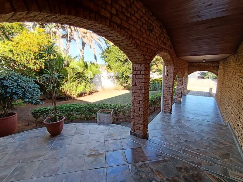 A covered patio featuring rustic brick arches, tiled flooring, and a timber-clad ceiling, overlooking a landscaped garden area.