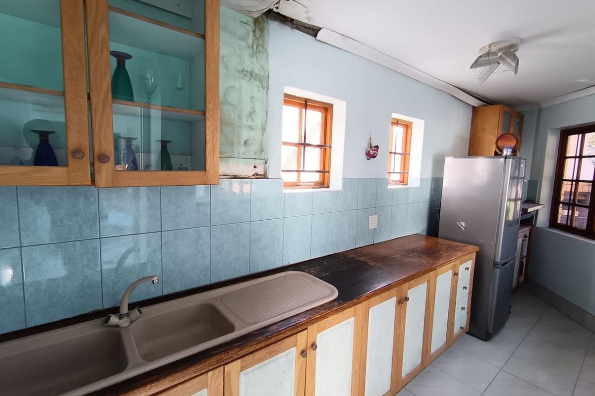 A dated kitchen featuring wooden cabinetry, tiled splashbacks, and a double sink, currently showing significant signs of ceiling water damage and wear.