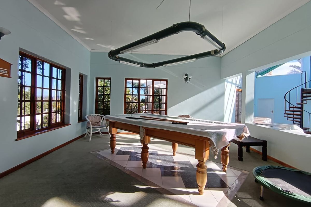 Spacious entertainment room featuring large wooden-framed windows, tiled inlay flooring, and a unique overhead lighting fixture, with direct access to an outdoor spiral staircase.