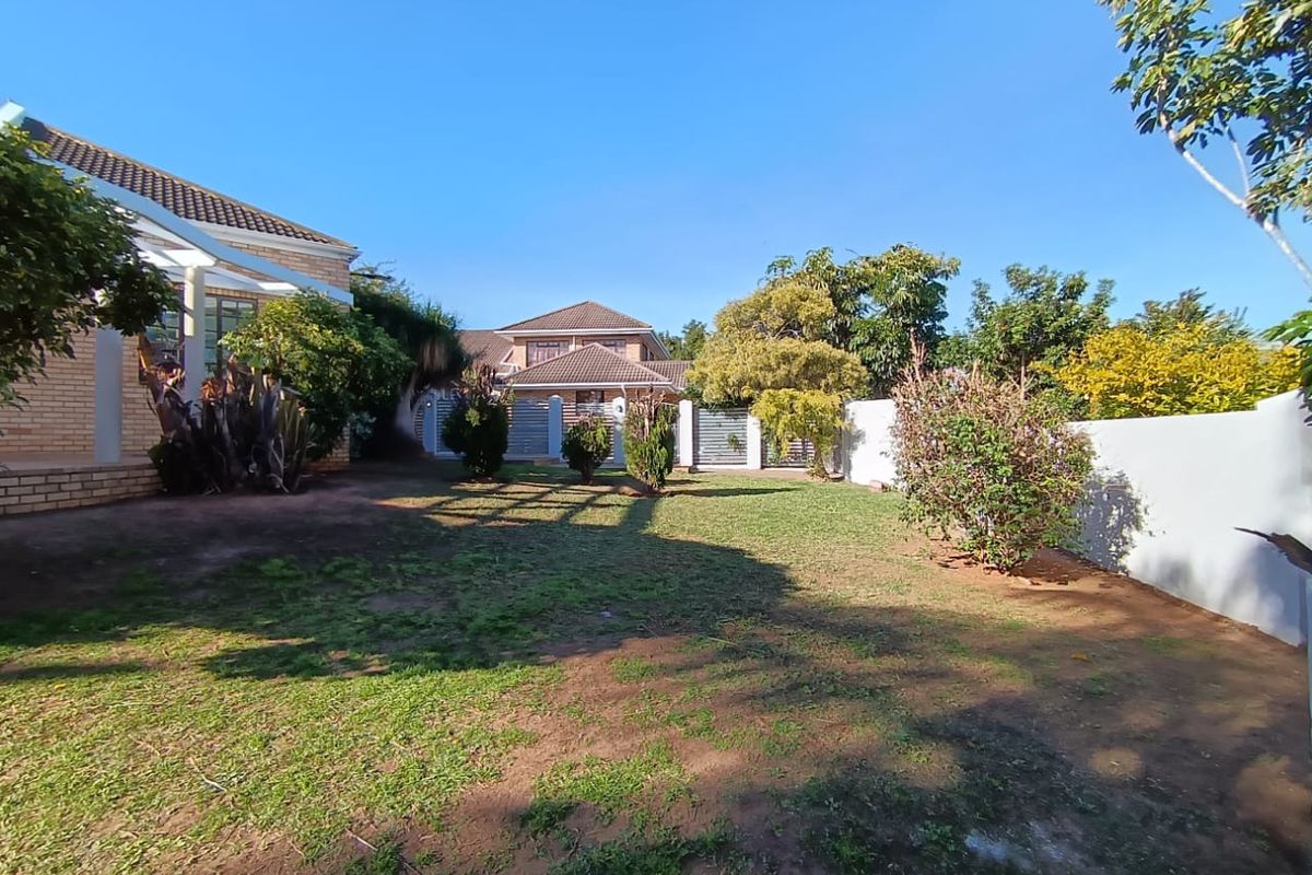 A spacious rear garden area featuring a lawn, established shrubs, and perimeter boundary walls, providing a private outdoor space.