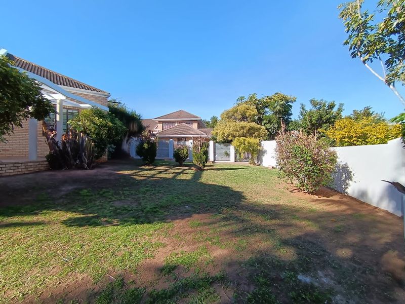 A spacious rear garden area featuring a lawn, established shrubs, and perimeter boundary walls, providing a private outdoor space.