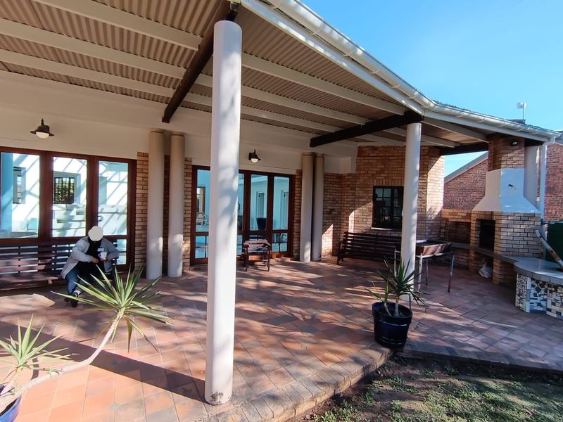 Covered outdoor patio featuring a built-in brick braai, tiled flooring, and structural support columns, ideal for alfresco dining and entertaining.