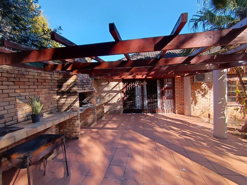 Covered outdoor patio featuring a built-in brick braai and fireplace, timber pergola structure, and tiled flooring, ideal for alfresco entertaining.