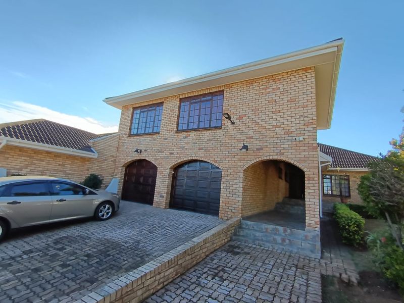 A two-story face-brick house featuring a double garage, arched entryway, and paved driveway, showcasing a classic architectural style with tiled roofing.