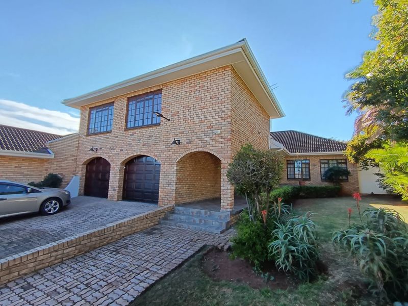 A well-maintained double-story face-brick house featuring a paved driveway, double garage, and an arched covered entrance with established garden landscaping.