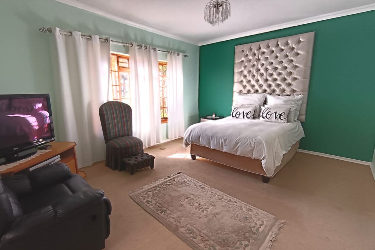 Spacious bedroom featuring a prominent green accent wall, neutral carpeting, and large windows allowing for natural light.