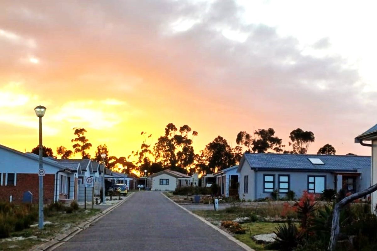 A scenic street view of a residential estate at sunset, featuring paved roads, street lighting, and established residential homes.