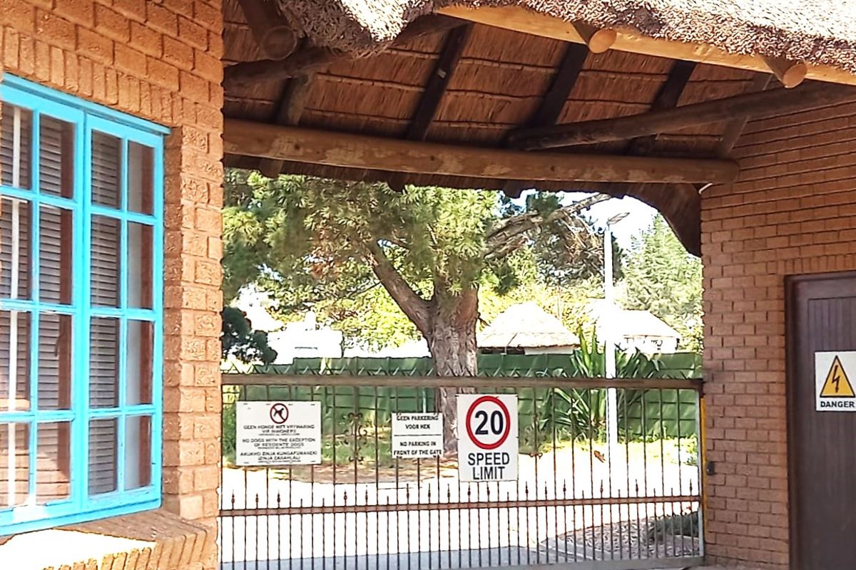 A gated entrance featuring a brick structure with a thatched roof, metal security gate, and signage.