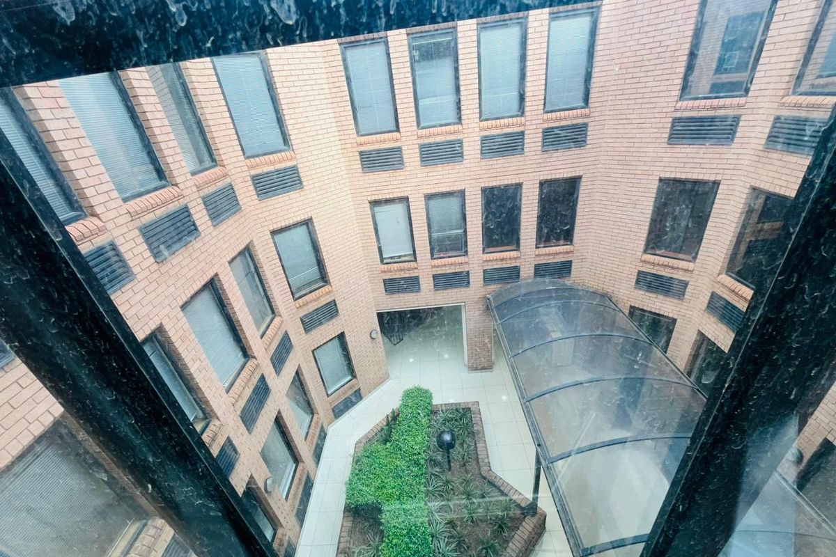 An elevated view of a commercial building courtyard featuring a central landscaped garden, tiled flooring, and a curved covered walkway.