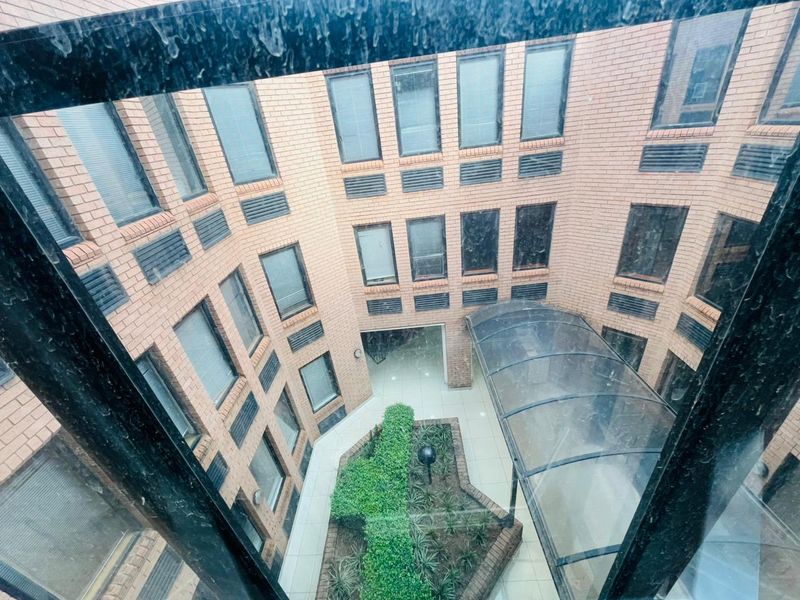 An elevated view of a commercial building courtyard featuring a central landscaped garden, tiled flooring, and a curved covered walkway.