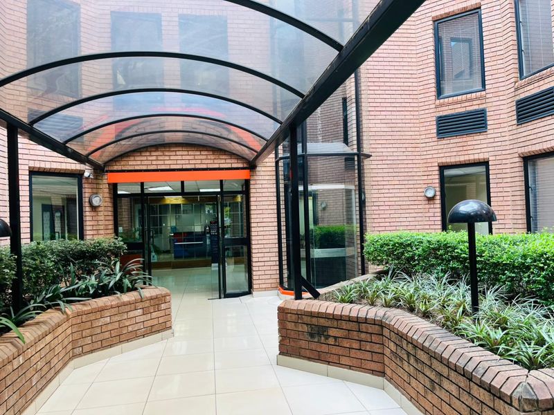 A well-maintained commercial entrance featuring a brick facade, a covered walkway with a curved awning, and landscaped brick planter boxes.