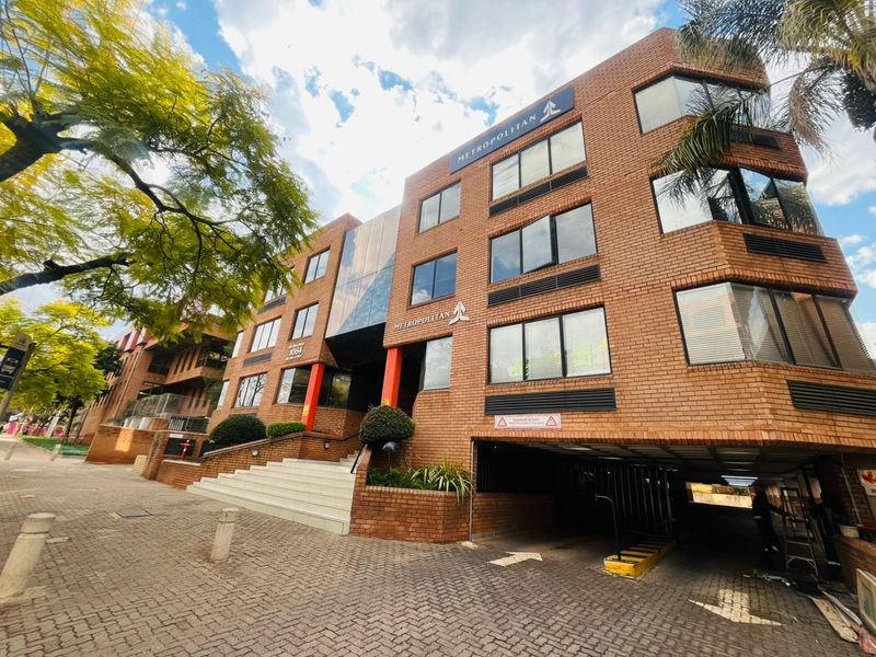 A multi-story commercial brick building featuring a paved entrance, staircase access, and an integrated undercover parking area.
