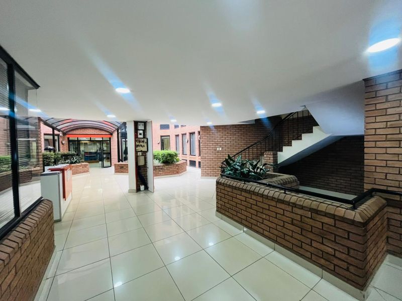 A bright, modern commercial building entrance featuring exposed brick walls, polished tile flooring, and a central staircase leading to upper levels.