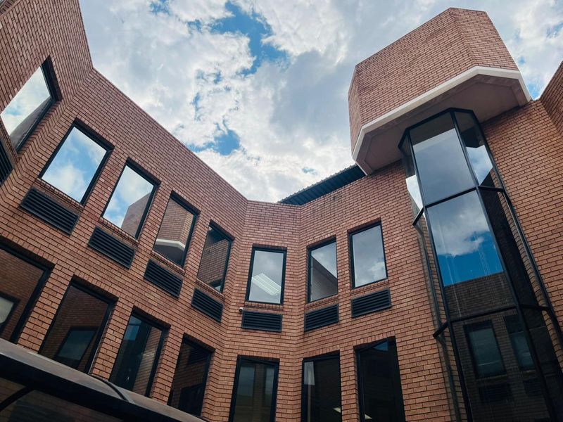 A low-angle view of a multi-story commercial building featuring a red brick facade, large glass windows, and integrated ventilation systems.