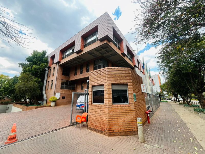Exterior view of a multi-story commercial building featuring a brick facade, a dedicated security guard booth, and a paved entrance area.