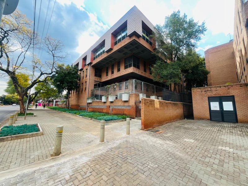 A multi-story commercial building featuring a brick facade, metal window frames, and a paved street-level entrance with perimeter security fencing.