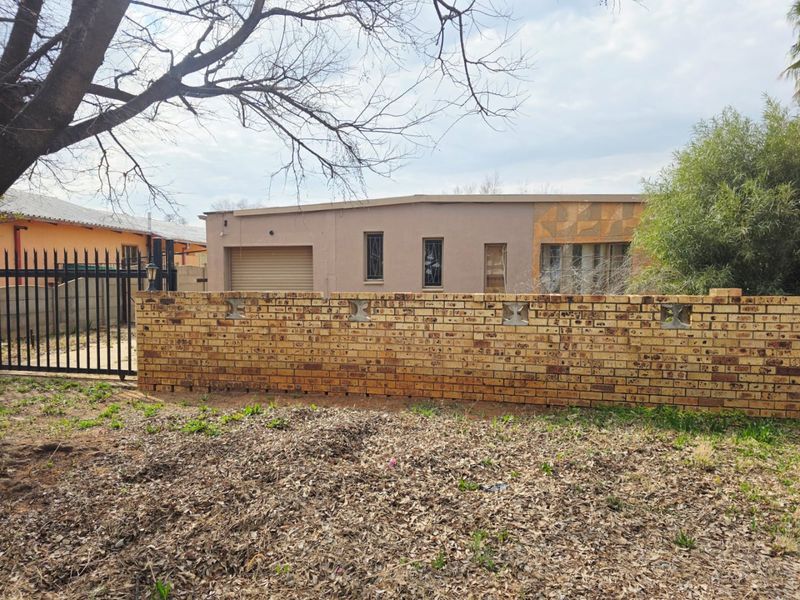 Front view of a single-story house featuring a face brick boundary wall, metal security gate, and a garage with a roller door.