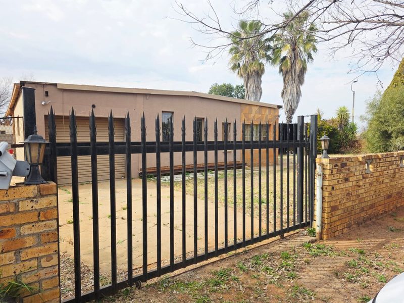 Front view of the property featuring a metal security gate, brick boundary wall, and paved driveway leading to a single garage.