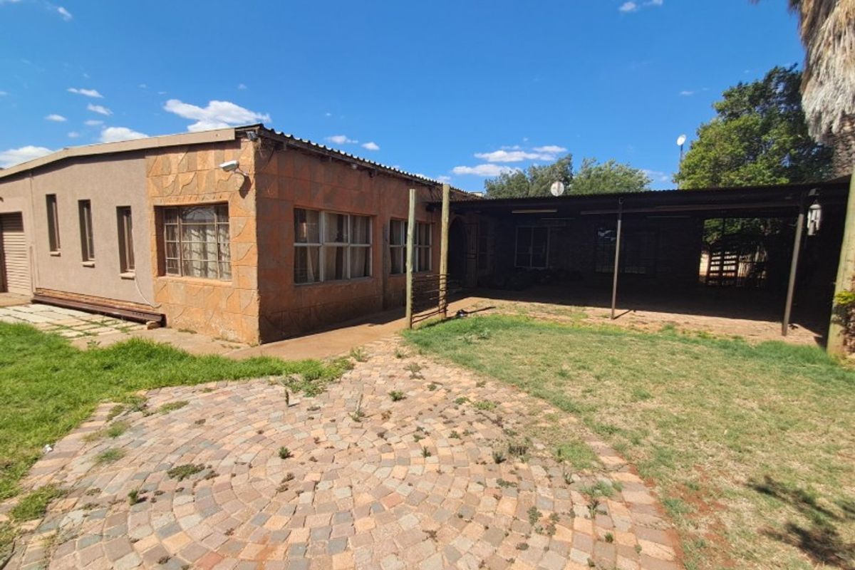 Rear exterior view of the house featuring a covered patio area, stone-clad facade, and a paved garden space requiring maintenance.
