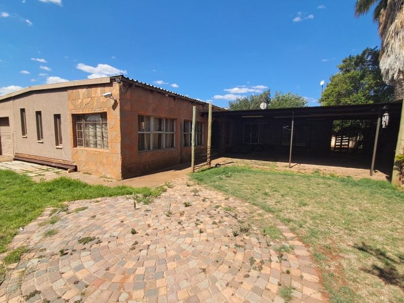 Rear exterior view of the house featuring a covered patio area, stone-clad facade, and a paved garden space requiring maintenance.