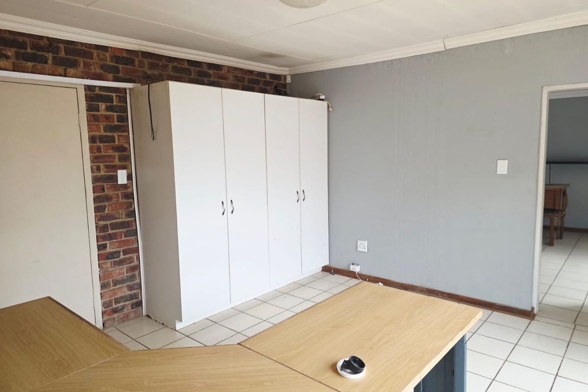 Bedroom featuring built-in cupboards, tiled flooring, and an exposed brick accent wall, offering a functional space with potential for cosmetic updates.