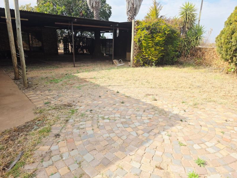 Rear garden area featuring a covered patio with brick paving and a metal roof structure, requiring landscaping and maintenance.