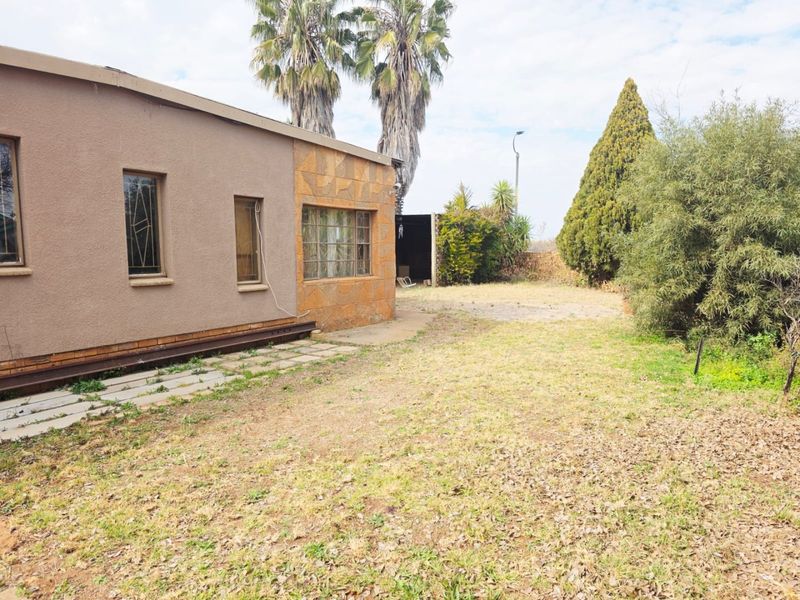 Rear view of the property featuring stone cladding accents, security bars on windows, and a large, dry garden area.