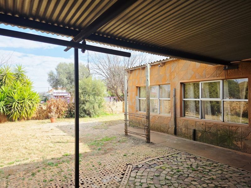 A covered outdoor patio area featuring stone-clad exterior walls, a corrugated metal roof, and paved flooring overlooking the garden.