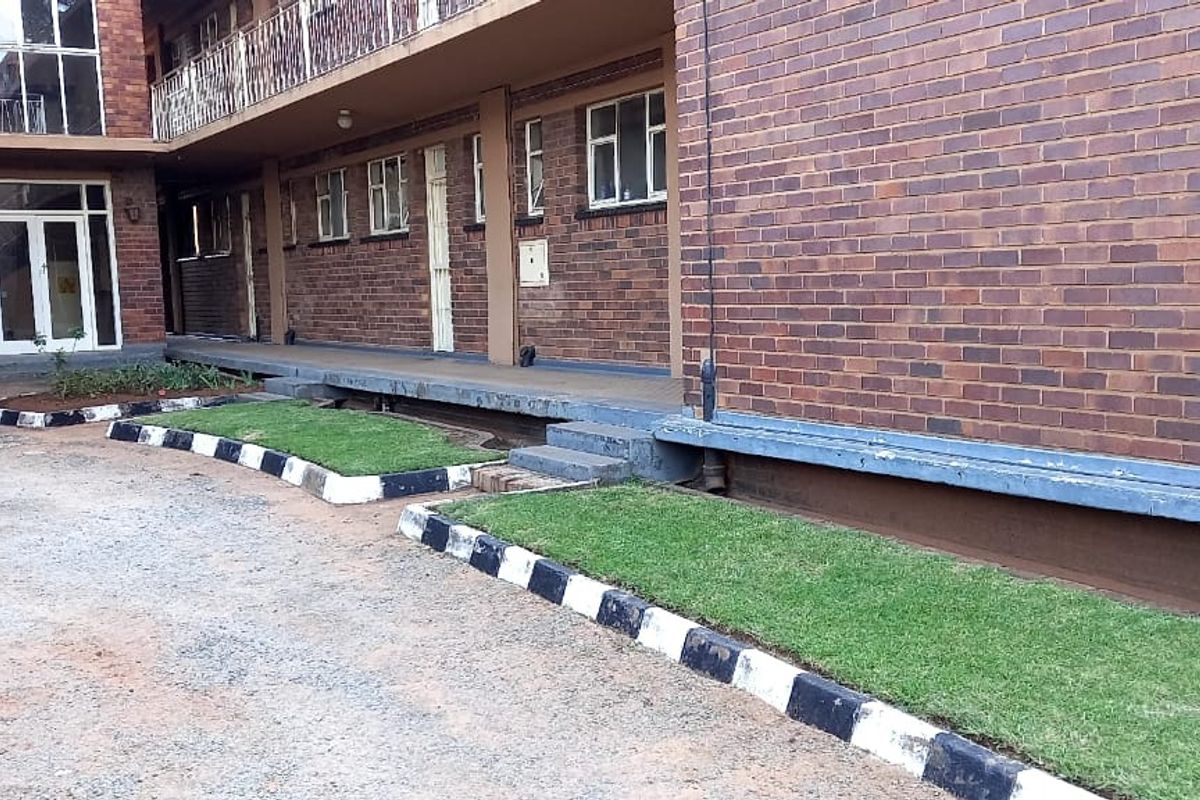 Exterior view of an apartment building featuring a face brick facade, paved driveway, and landscaped lawn borders with concrete kerbing.