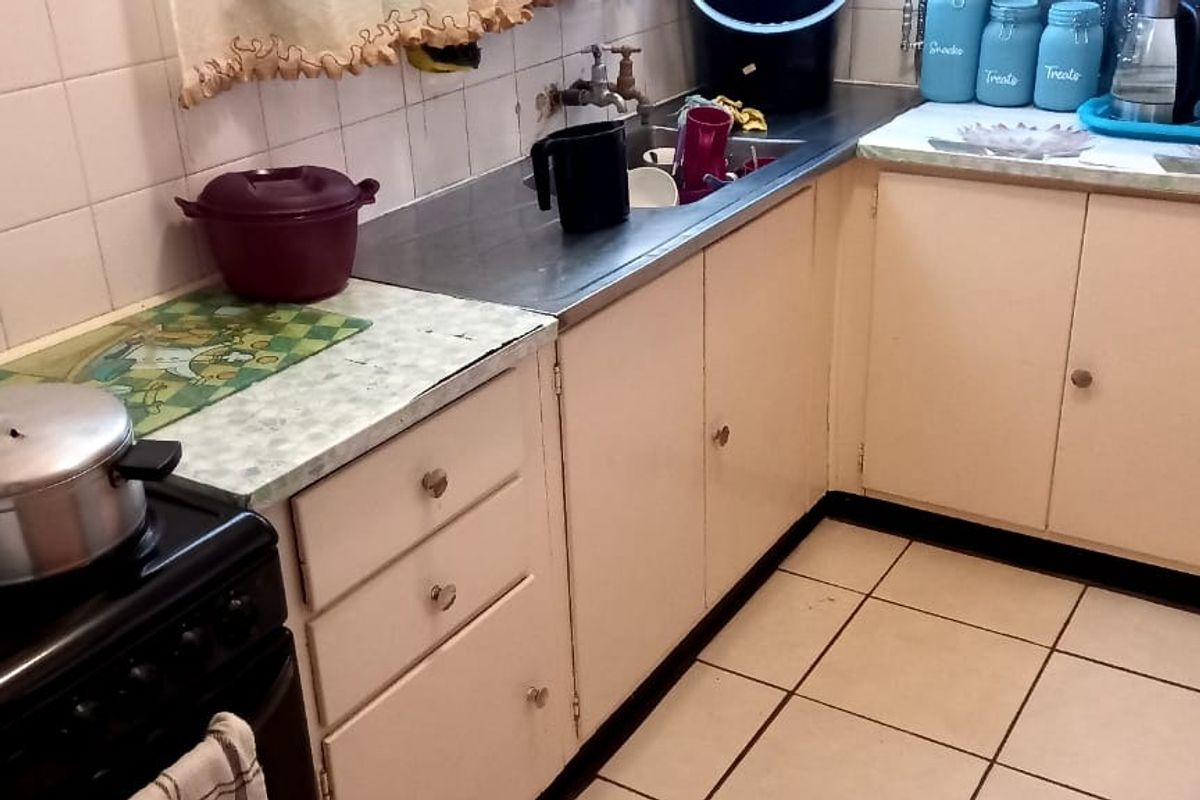 A functional kitchen featuring dated cabinetry, laminate countertops, a stainless steel sink, and ceramic floor tiles, offering potential for a modern renovation.