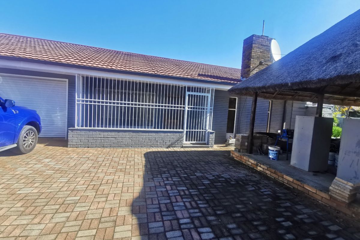 Exterior view of the property featuring a paved driveway, a garage, security bars, and a thatched outdoor entertainment area with a built-in chimney.