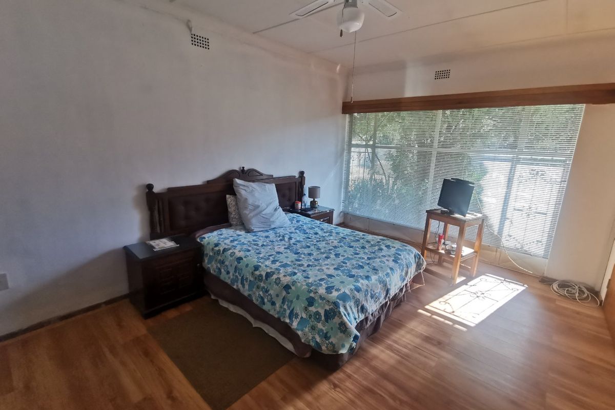 A spacious bedroom featuring wood-look flooring, a ceiling fan, and large windows with fitted blinds, offering a functional and well-lit living space.