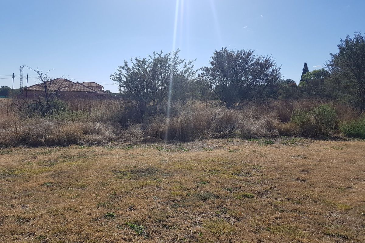A view of a vacant residential plot featuring natural vegetation and dry grass, suitable for future development.