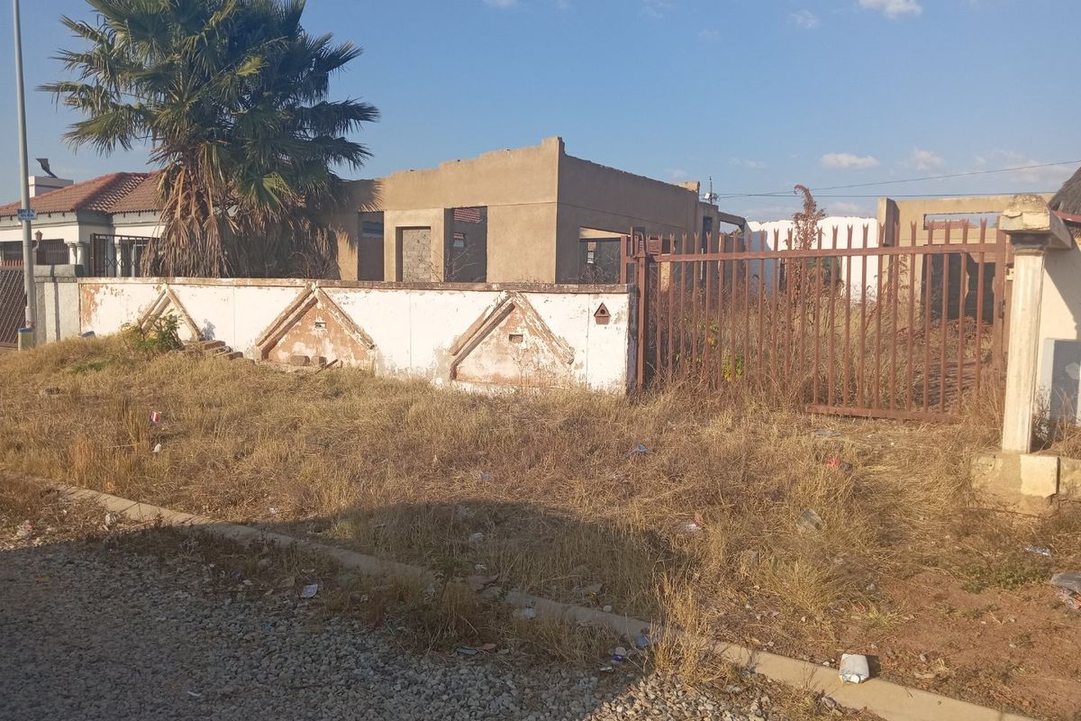 A vacant residential plot featuring an unfinished building structure, a weathered perimeter wall, and overgrown grounds, offering potential for development.