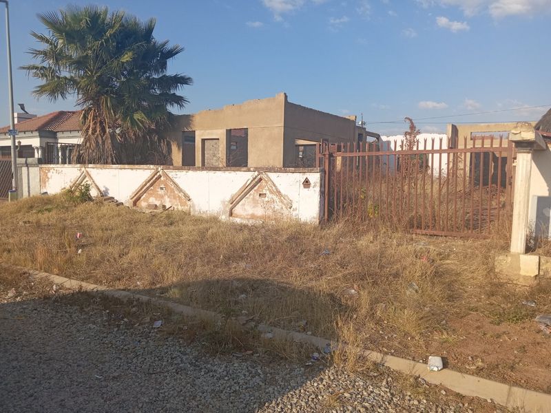 A vacant residential plot featuring an unfinished building structure, a weathered perimeter wall, and overgrown grounds, offering potential for development.